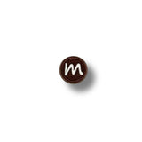 Parche bordado redondo con letra “m” en blanco sobre fondo marrón chocolate, estilo sencillo y limpio.