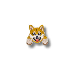Primer plano de parche bordado con diseño de perro Shiba Inu, lengua afuera y expresión alegre.