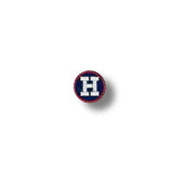 Parche circular con la letra "H" bordada en blanco sobre fondo azul marino, borde rojo fino.