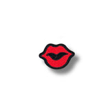Imagen de un parche bordado con forma de labios rojos delineados en negro, acabado mate y diseño compacto.