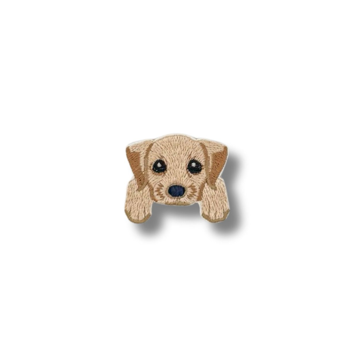Primer plano de un parche bordado con el rostro de un cachorro labrador en tonos beige claro, ojos grandes y expresivos.