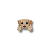 Primer plano de un parche bordado con el rostro de un cachorro labrador en tonos beige claro, ojos grandes y expresivos.