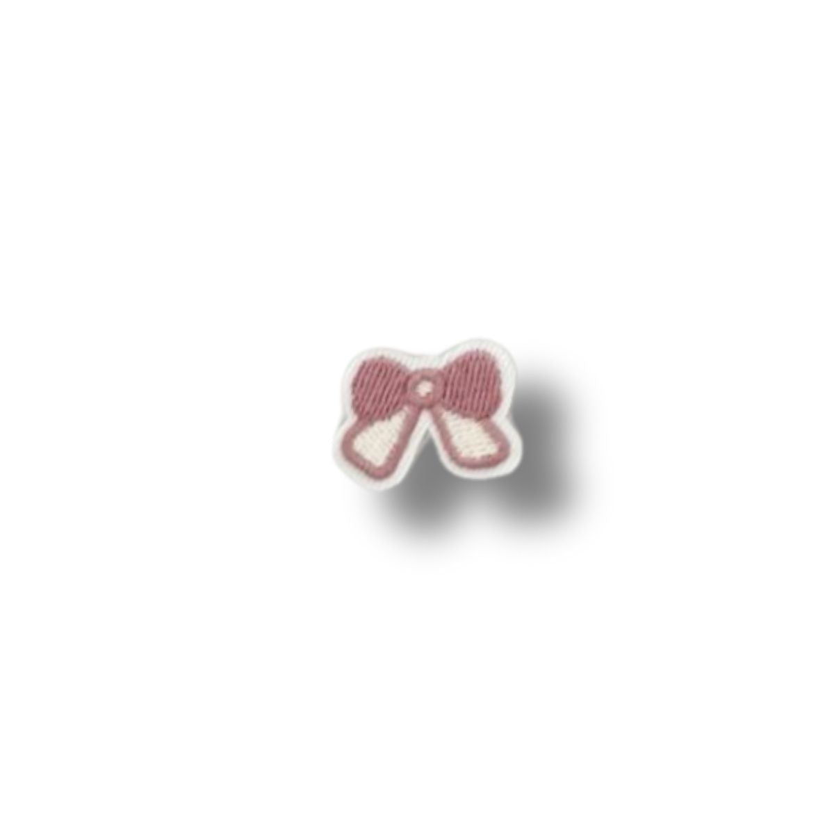Parche bordado en forma de lazo rosa pastel con contorno blanco, diseño delicado y femenino sobre fondo blanco.