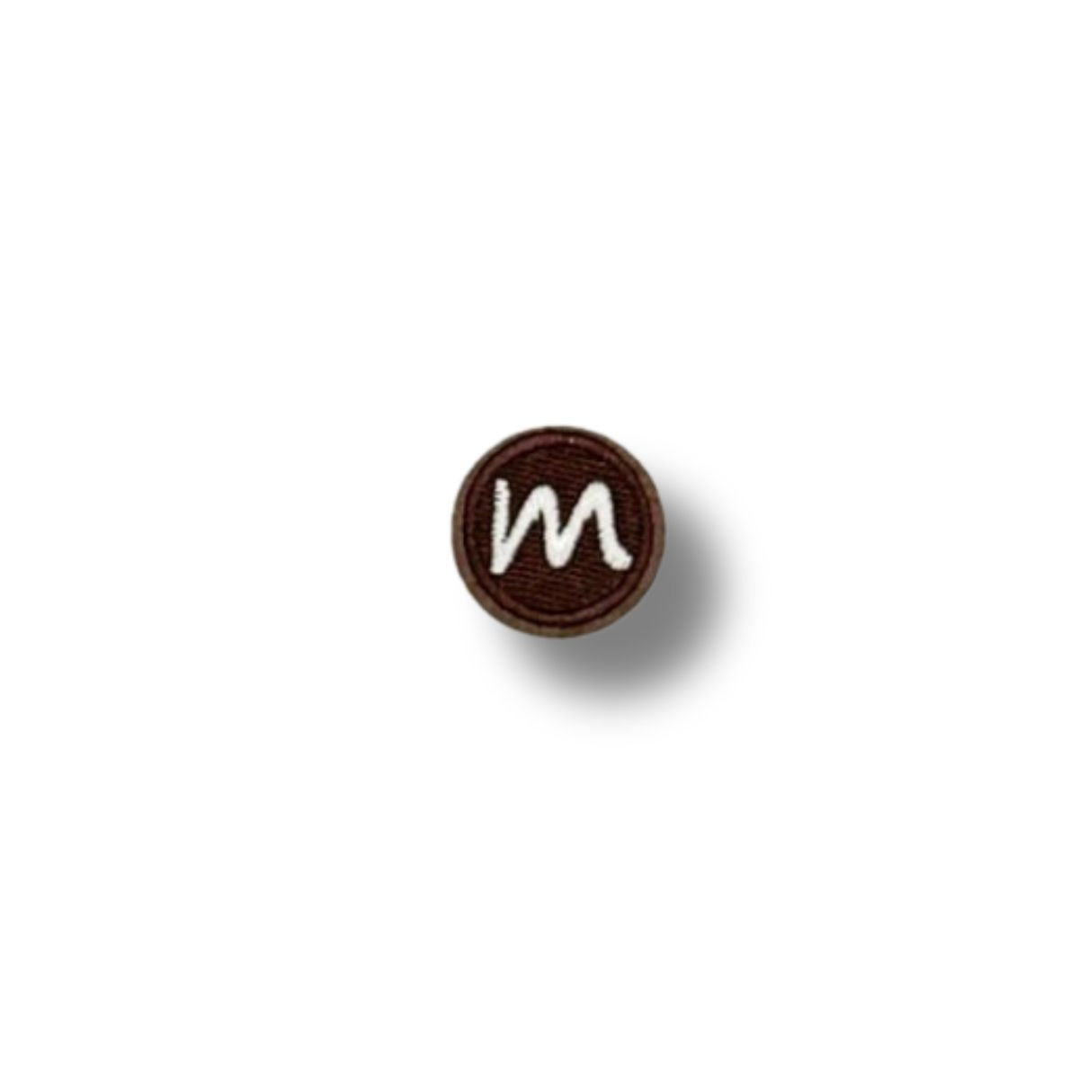 Parche bordado redondo con letra “m” en blanco sobre fondo marrón chocolate, estilo sencillo y limpio.