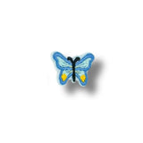 Parche bordado con forma de mariposa azul claro con detalles celestes y puntos amarillos, diseño simétrico y contorno blanco.