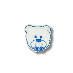 Primer plano de parche bordado con cabeza de osito blanco y detalles en azul, incluyendo un moño decorativo.